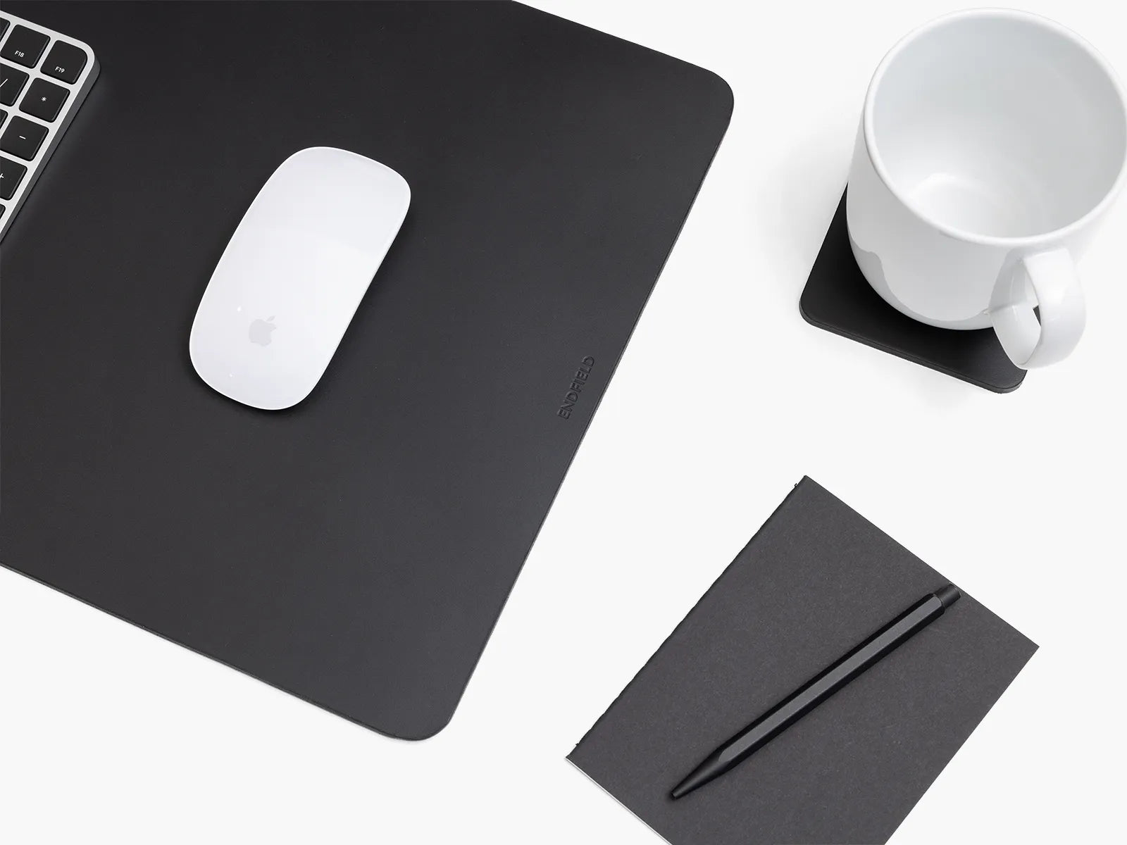 Black leather desk mat with a mouse, pen, and mug on a white surface.