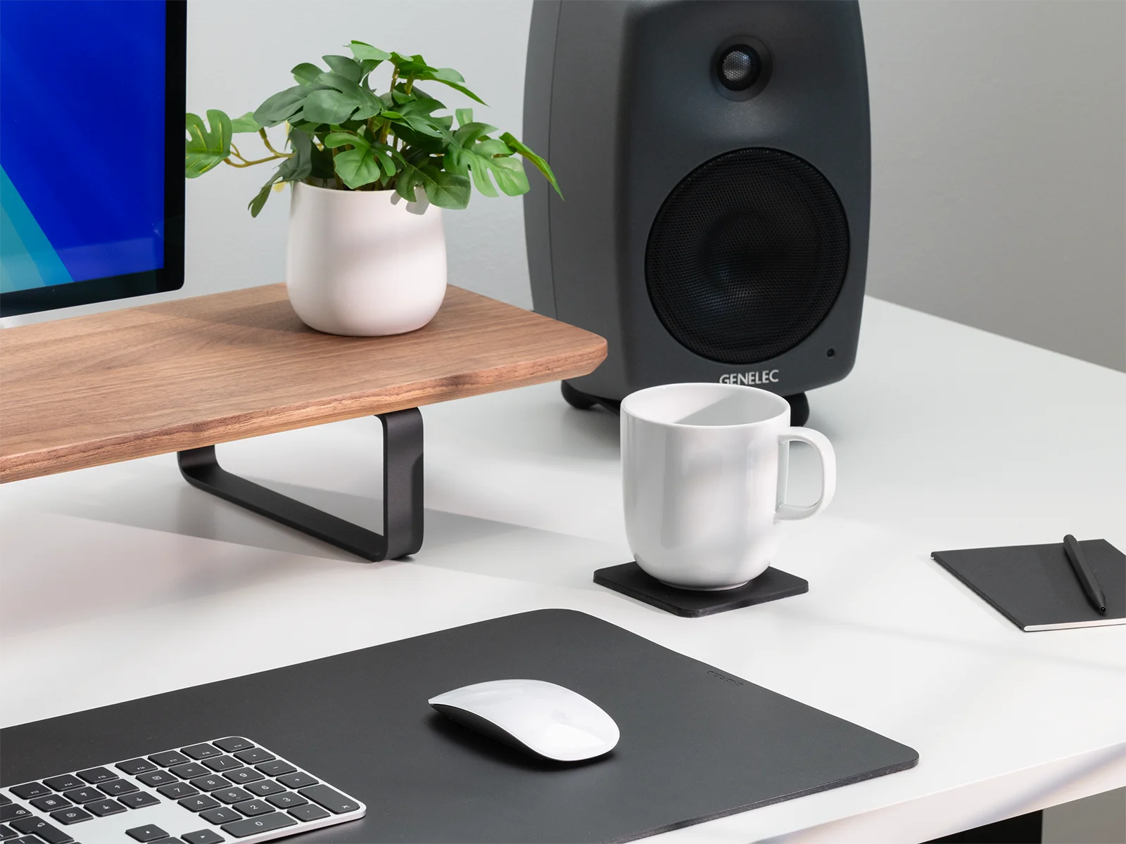 Modern office desk setup with computer monitor, speakers, mug, mouse, and plant.