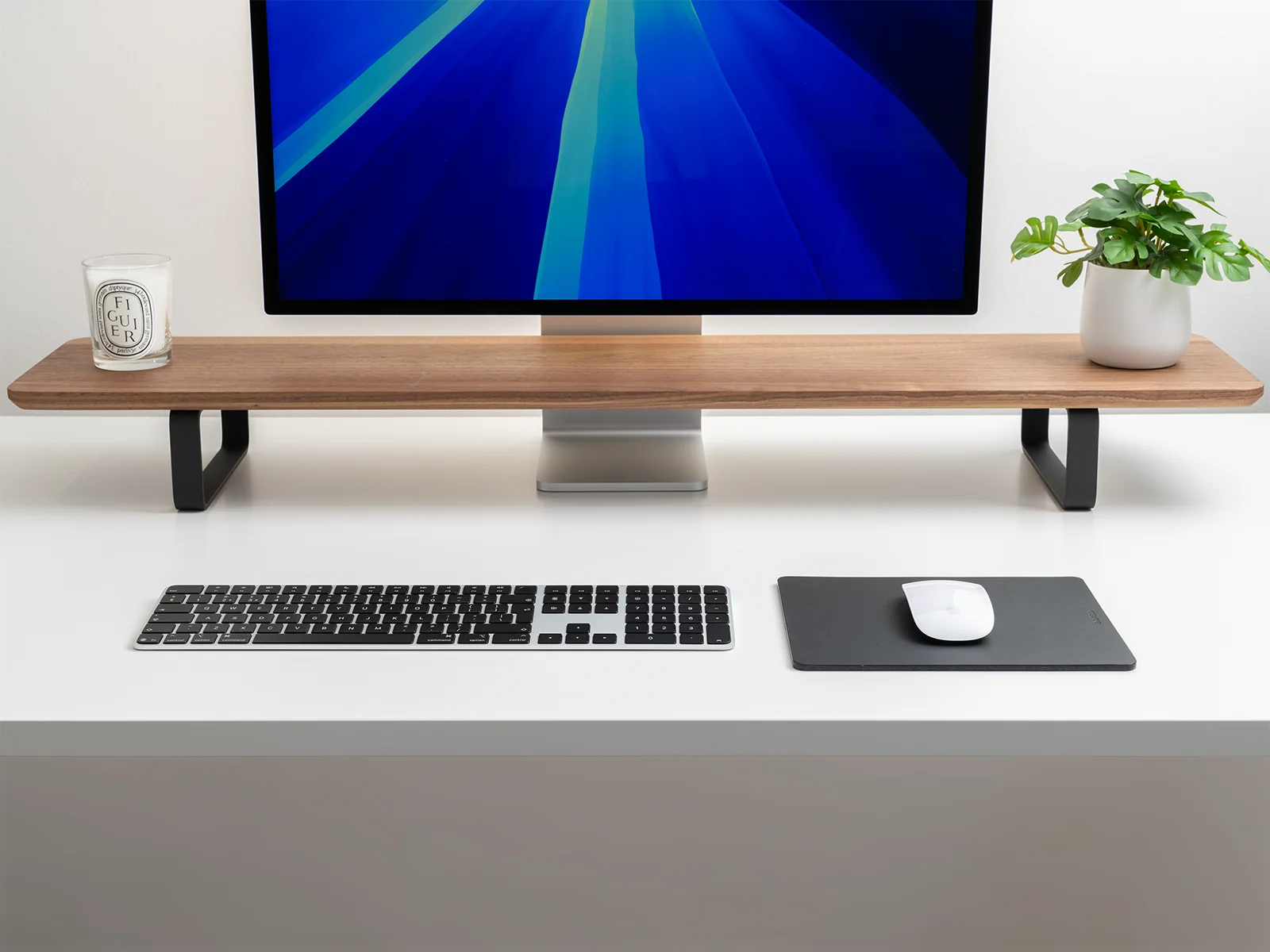Modern desk setup with a black leather mouse pad, keyboard, monitor and shelf.